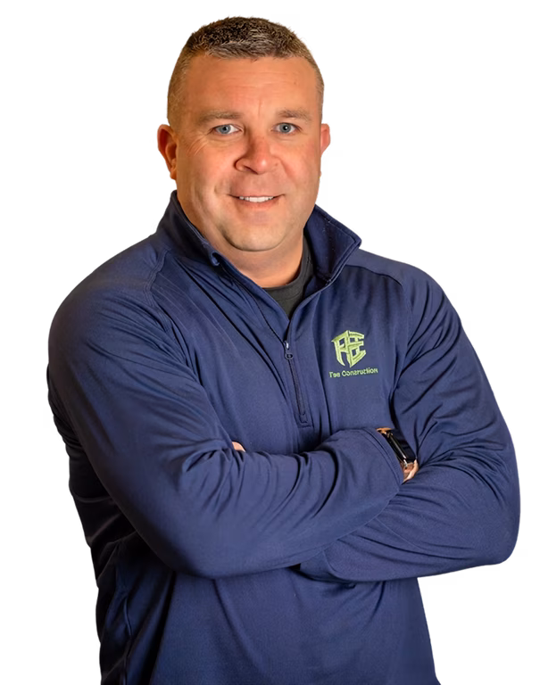 Portrait of a smiling man with crossed arms, wearing a navy jacket with a green logo, posed against a black background with a confident tone.