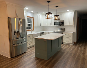 Modern white kitchen with stainless steel appliances, wood floors, and a dark green island beneath pendant lights; bright, clean, and welcoming.