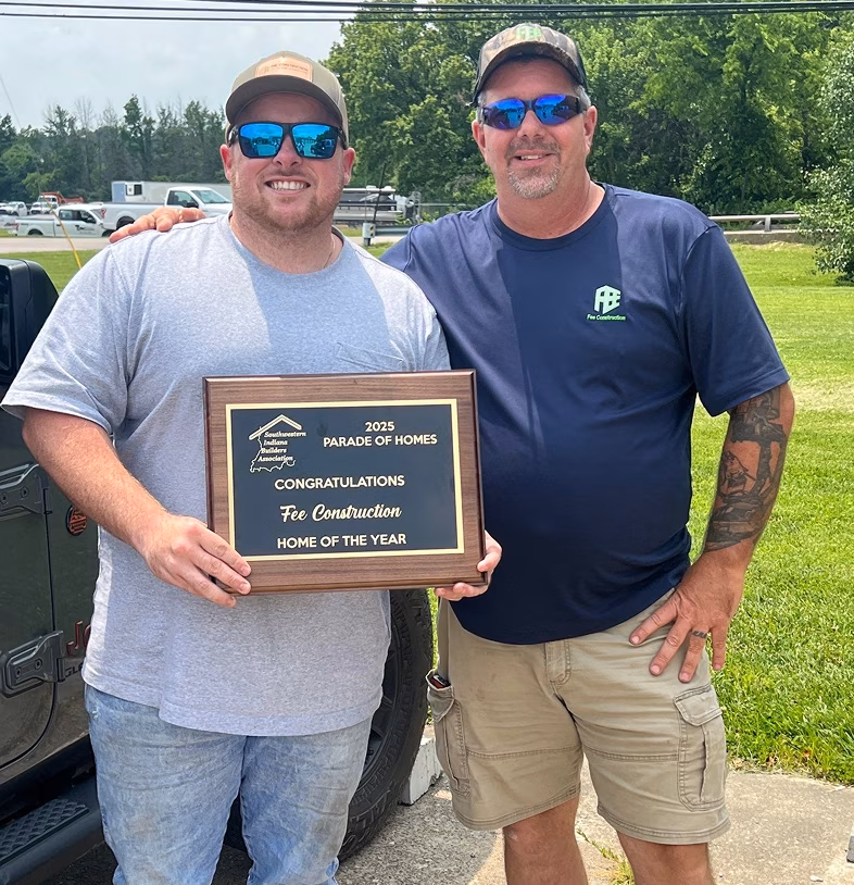 Two smiling men in sunglasses pose outdoors, holding a plaque naming Fee Construction “Home of the Year” at the 2025 Parade of Homes. A proud, celebratory moment.