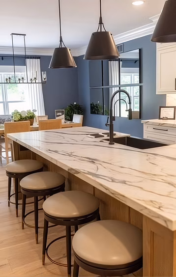 Modern blue-and-white kitchen with a marble waterfall island, four tan stools, black pendant lights, and a farmhouse sink, creating a warm, stylish feel.