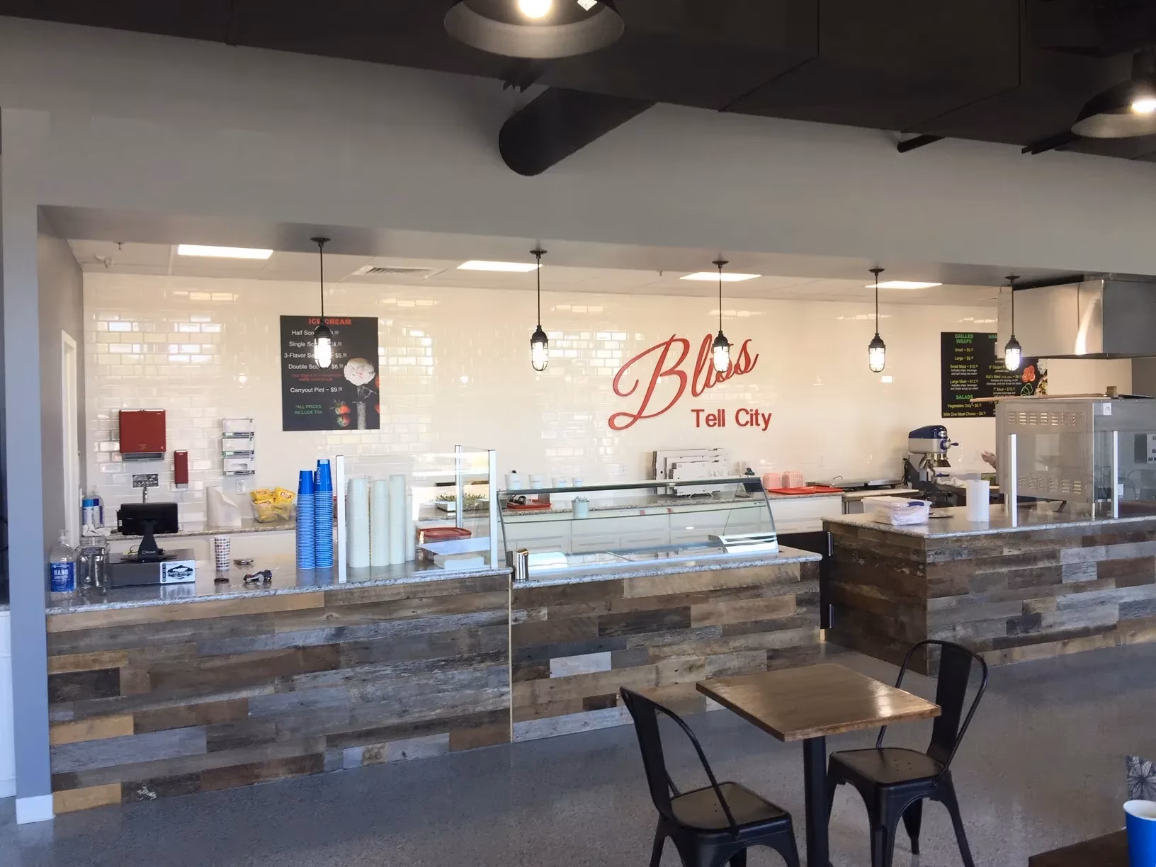 Bright, modern Bliss Tea City bubble tea café with a long wood-fronted service counter, glass display case, drink supplies, and small tables.