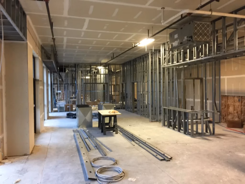 An unfinished commercial interior with exposed steel framing, drywall, metal tracks and coiled cables on the concrete floor; quiet, work-in-progress atmosphere.