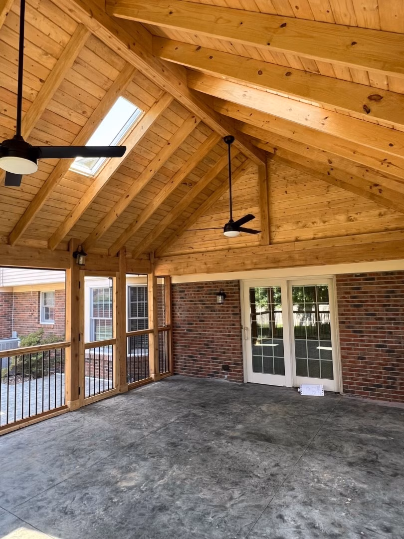 Spacious covered patio with a high, exposed timber ceiling, skylight, and two ceiling fans; brick walls, glass doors, and concrete flooring create a warm, open feel.