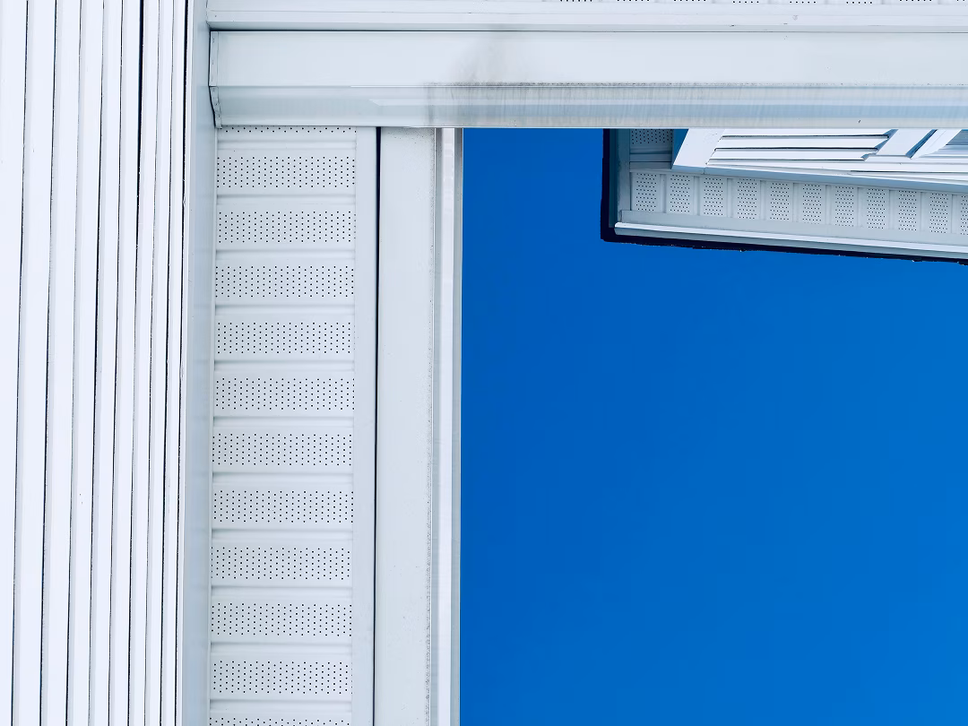 White house siding and perforated soffits frame a vivid blue sky, creating a crisp, minimalist architectural scene with a calm, airy feel.
